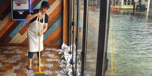 A woman sweeps up a flooded business