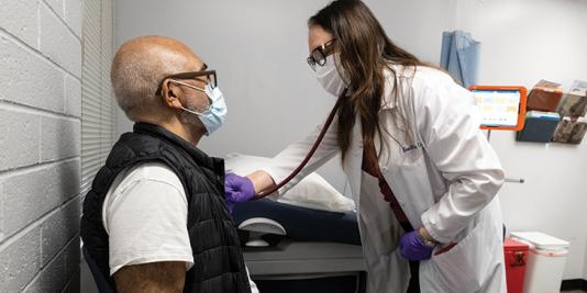 Physician checks man's heartbeat with stethoscope.